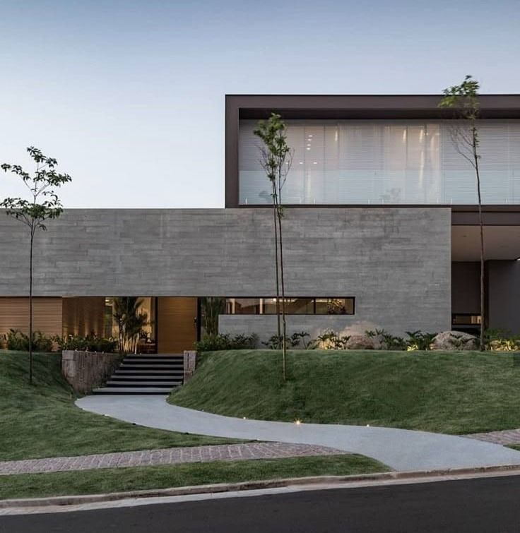 Casa con un largo muro de hormigón visto y una planta alta de vidrio iluminada al atardecer